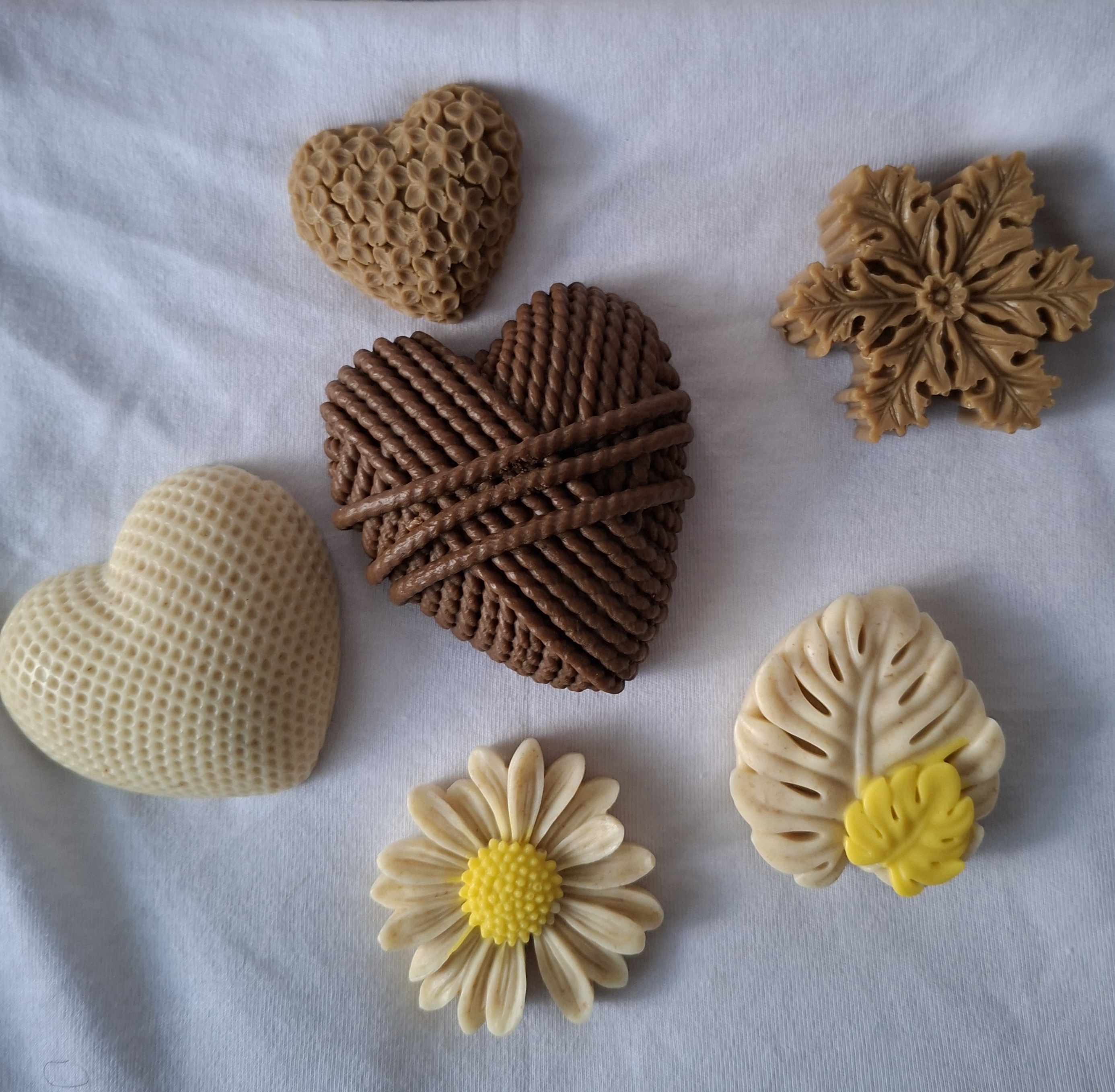    Variedad de jabones artesanales naturales en tonos terrosos y colores suaves, dispuestos sobre superficie de madera con hojas y flores secas